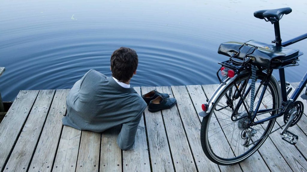 Foto de um executivo sentado em um pier e ao lado uma bicicleta para simular administração do tempo