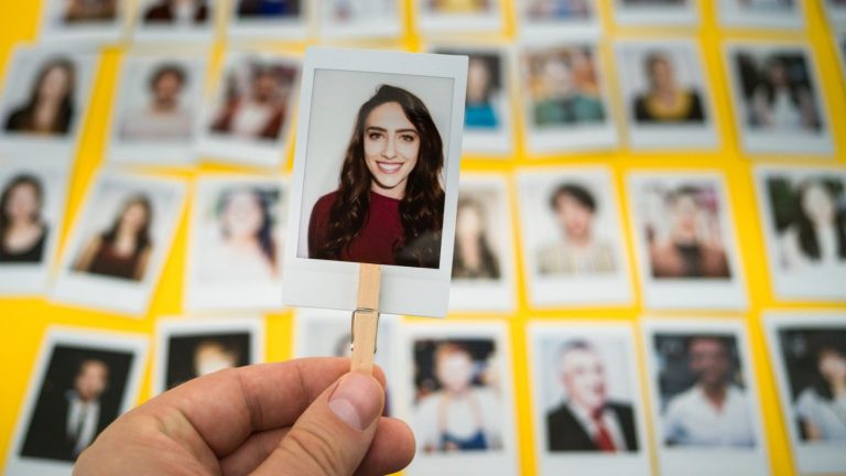 mão segurando uma foto 3x4 e ao fundo várias fotos uma ao lado da outra simulando o processo de Recrutamento e seleção