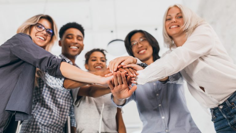 Foto de um grupo de pessoas com as mão uma em cima da outra no centro da imagem, simbolizando Gestão Humanizada