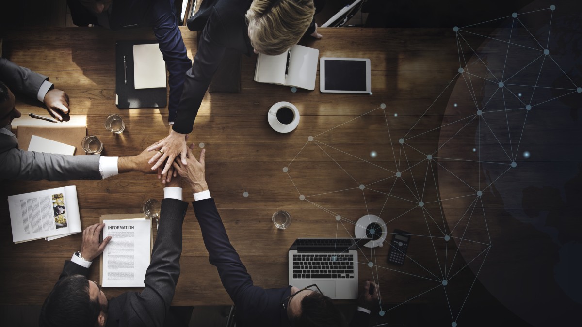 foto tirada de cima com uma mesa ao fundo e mão apoiadas umas em cima das outras para simular a liderança inclusiva