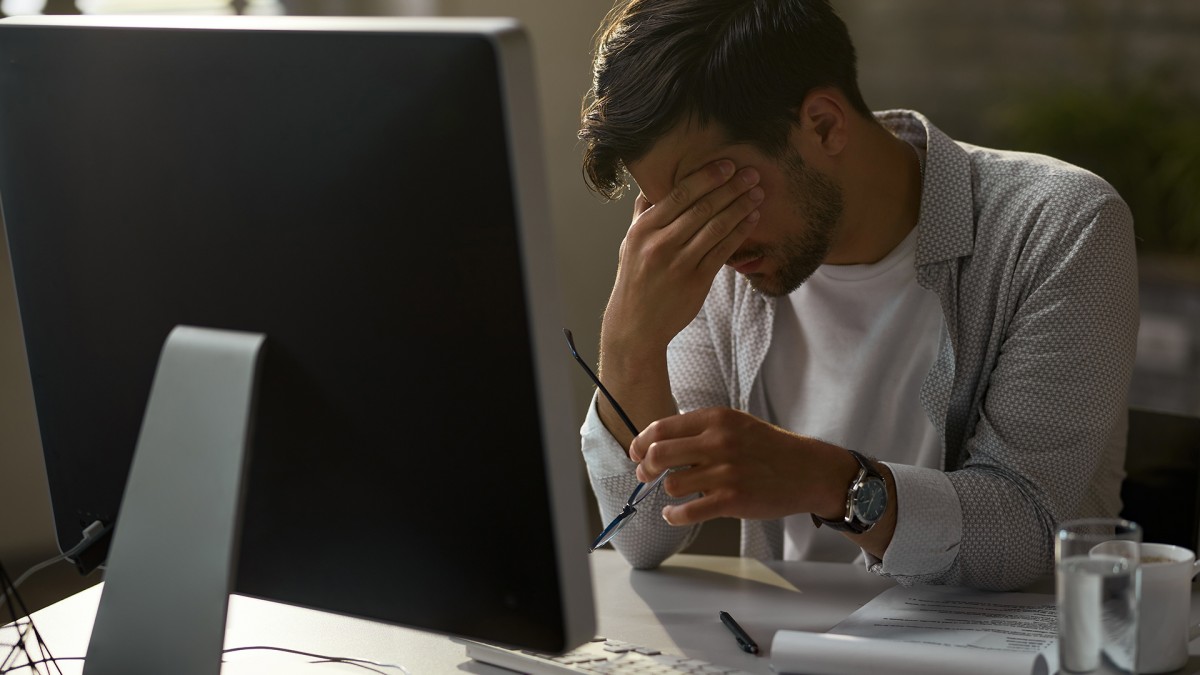 Foto de um homem em frente á um computador com a mão no rosto com gesto de cansado para simbolizar o quiet quiting