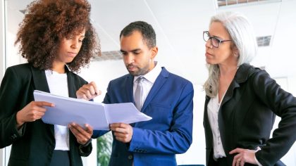 Há três executivos na imagem, o homem confere o trabalho realizado pelas duas mulheres