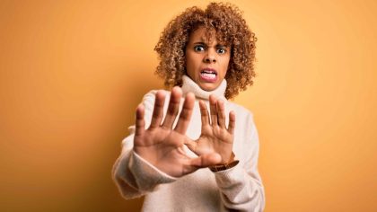 Mulher negra em fundo laranja com gestos de afastarmento, exprimindo a sensação de resistência à mudança