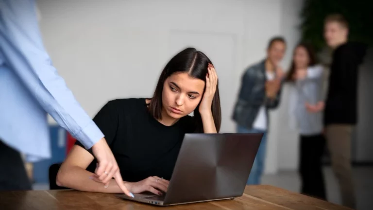 Mulher preocupada em frente ao laptop enquanto é apontada negativamente pela gestora