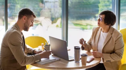 Em ambiente corporativo, uma mulher e um homem conversam, demonstrando estar em uma sessão de feedback entre líder (a mulher) e liderado (o homem)